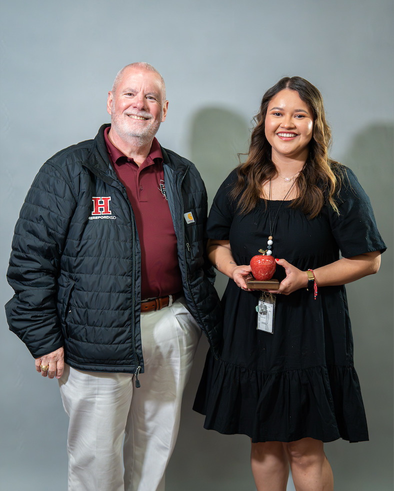 An older man and a woman standing next to each other. She holds an apple trophy.