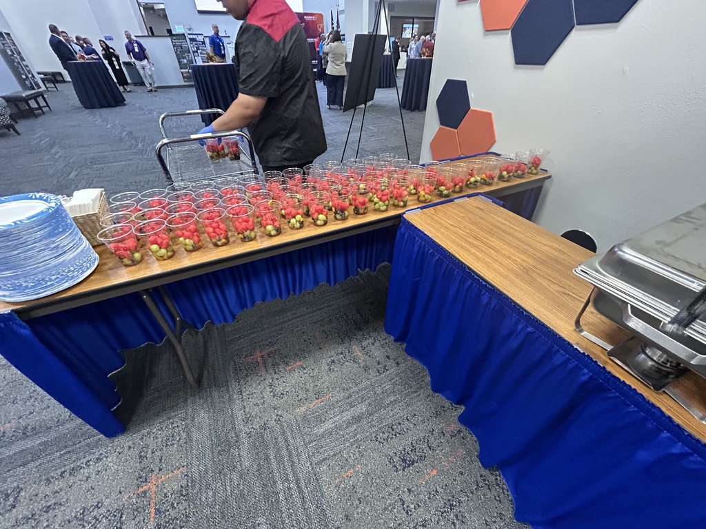 A person organizes food on a table, with a blue tablecloth, next to a wall with a geometric design.
