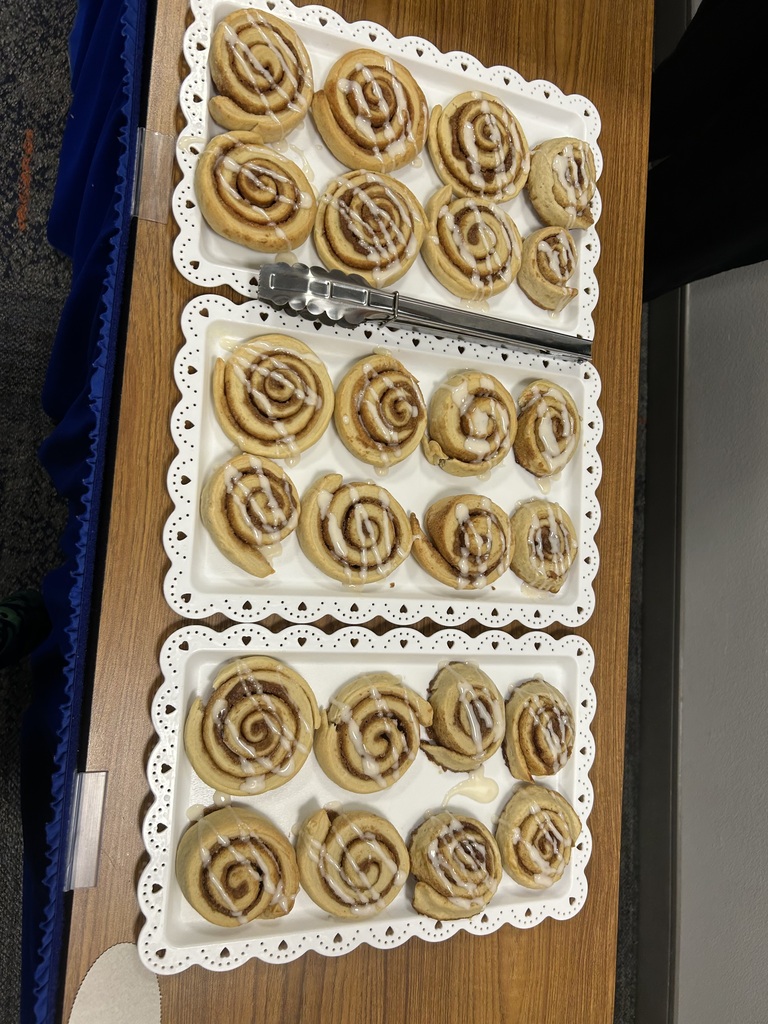 Two trays with cinnamon rolls on a wooden table. Trays are white with decorative edges.