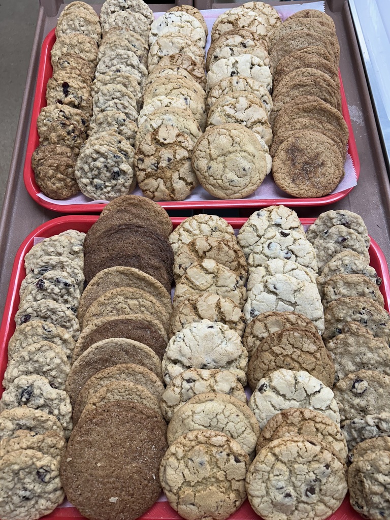Two trays of cookies are arranged on a table. Each tray contains multiple rows of cookies of various sizes and types.