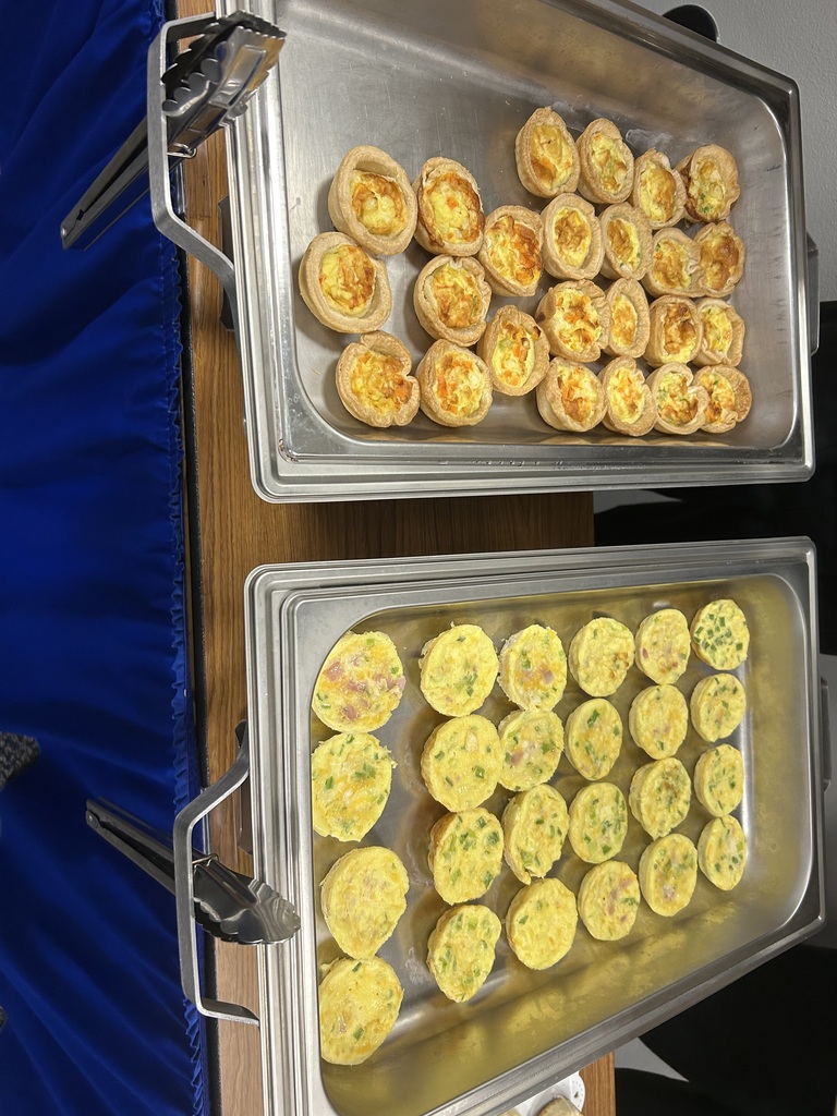 Two trays with lids hold multiple mini quiches, one with green vegetables and the other plain, on a table.