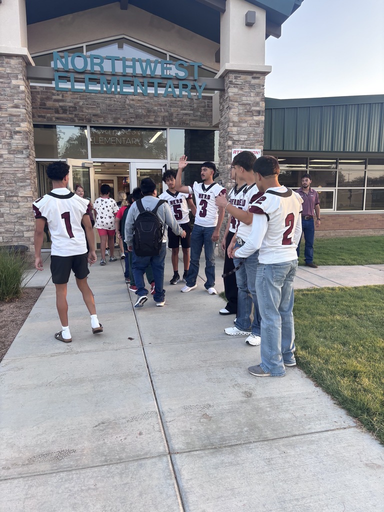 Several young people, including those in football jerseys, gather in front of a building. Some are conversing while others walk in the background.