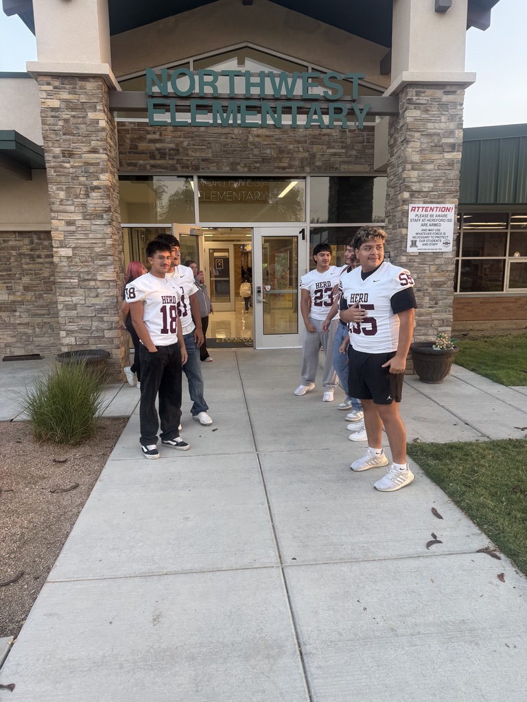 Five young men wearing football jerseys stand outside a school. One has the number 18, and the others have numbers 23, 45, and 55.