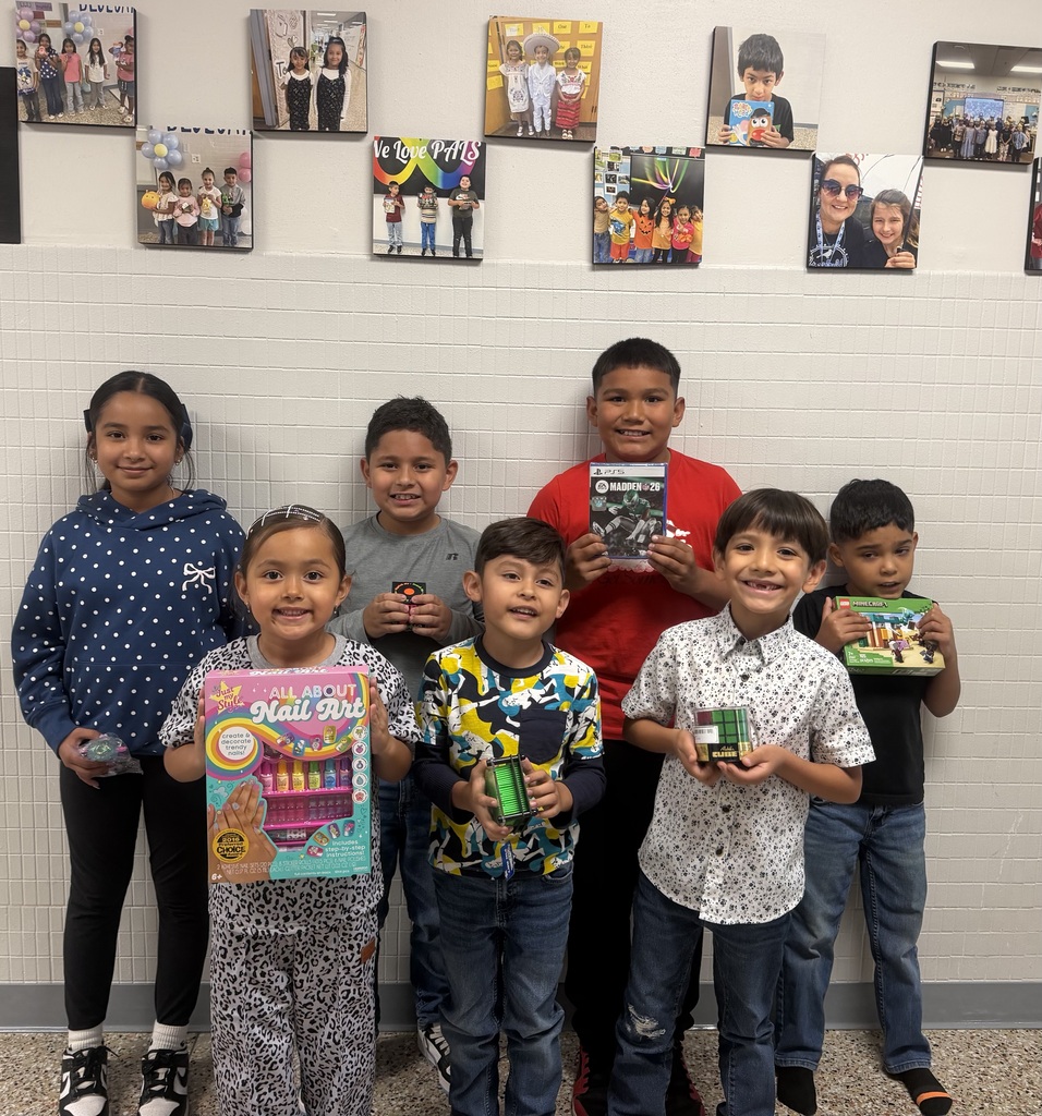 Children stand in a group holding items. A white wall with many pictures behind them.