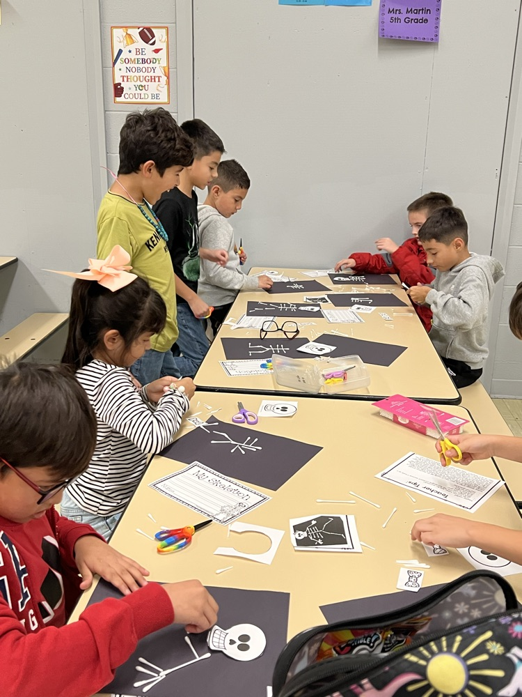 Students sitting at tables doing arts and crafts with paper, scissors, and coloring pencils.