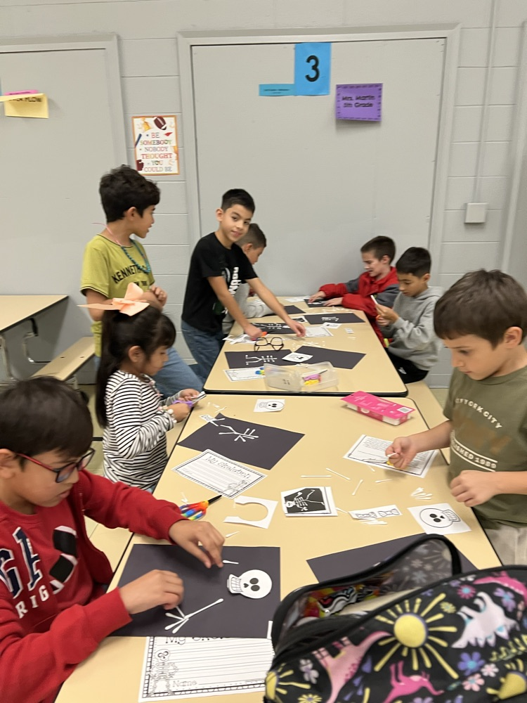 Children in a classroom with a number 3 on the wall are working on crafts at a table.