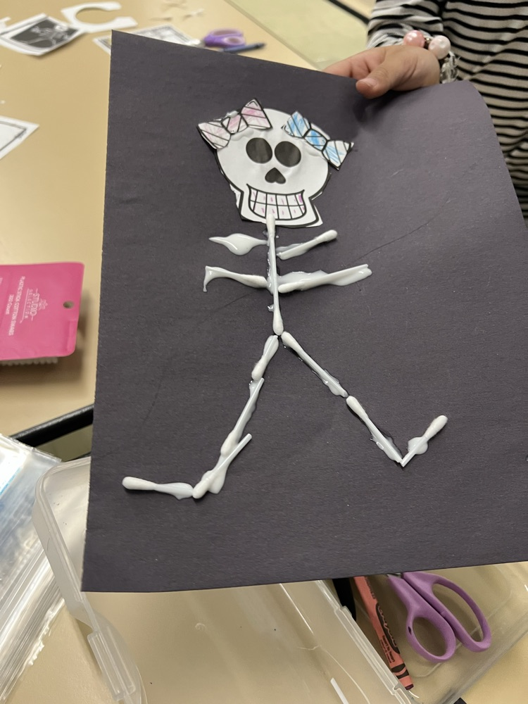 Hand holds a black paper with a skeleton figure made of white tape on a table.