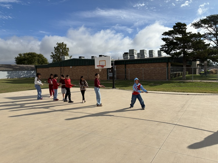 A group of children play on a basketball court. A building with brick walls is in the background.