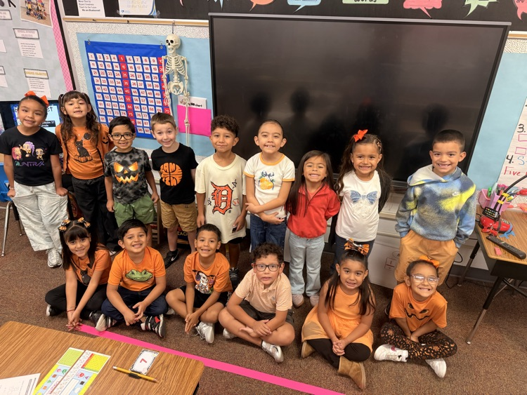 Classroom with children in various clothes, some wearing glasses, posing in front of a large monitor