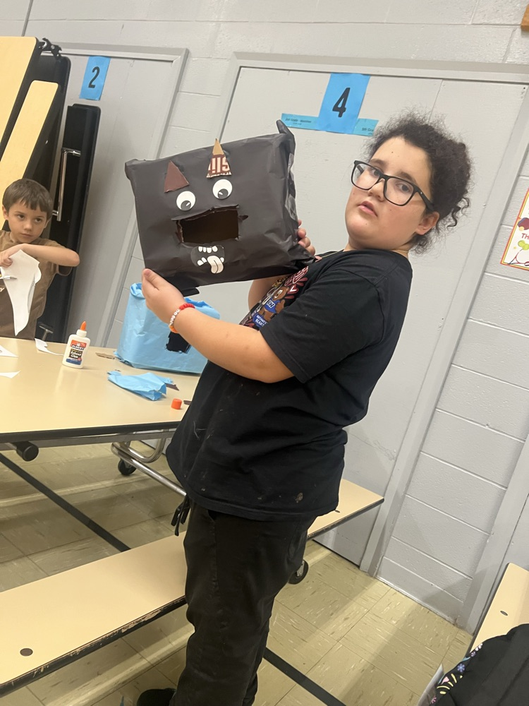A student holds up a brown bag with eyes, nose, and mouth drawn on it.