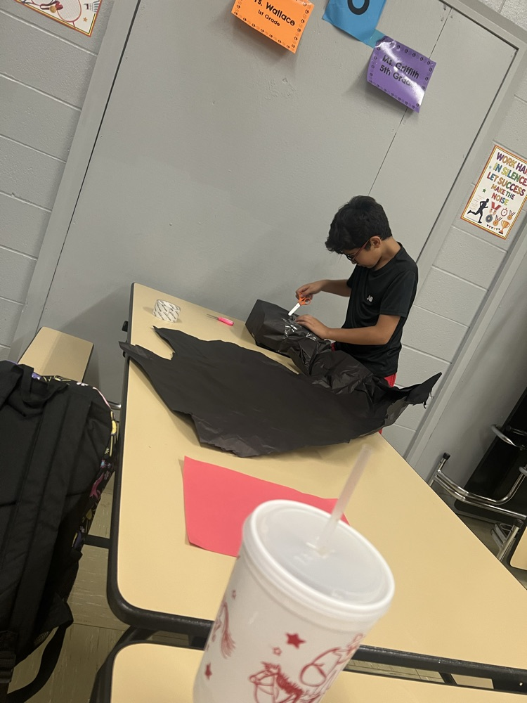 A student seated at a table, working on a black material with a pink item nearby.