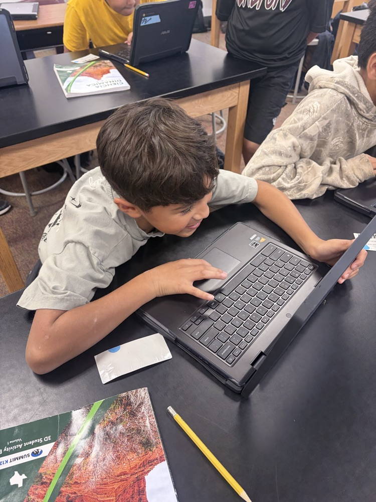 Two boys using laptops in a classroom, one lying on his side, and another sitting.