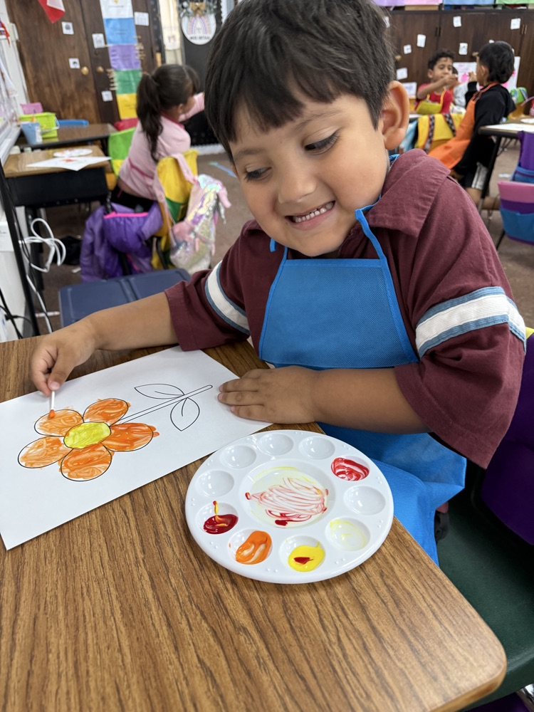 Boy painting a flower on paper with a palette of red, yellow, orange, and white paint.
