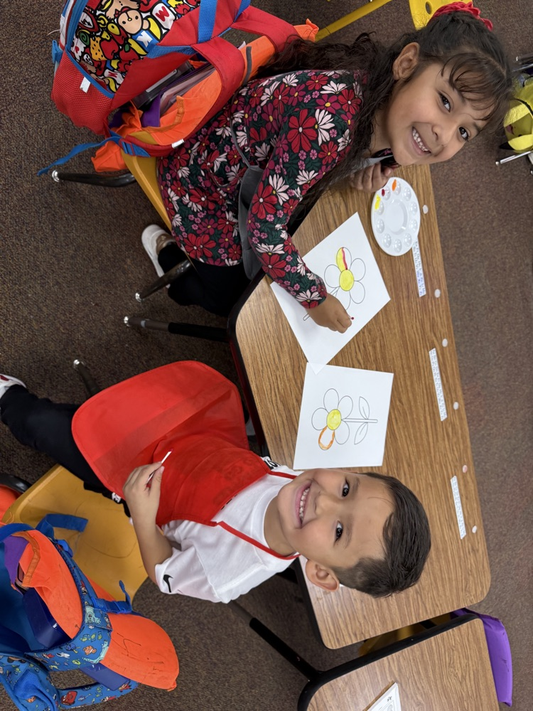 Two young children seated at a table. A girl draws on a piece of paper.
