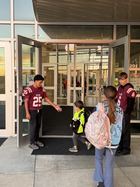 Members of the HMS railer football team greet elementary students as they arrive to school this morning.