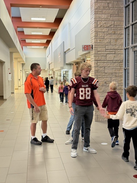 Coach Batchman and a few HMS railer football players greet students in the HES hallway this morning as they walk to breakfast.