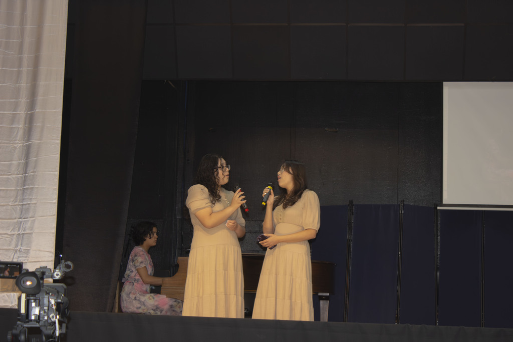 two sisters singing on stage with a pianist in the background