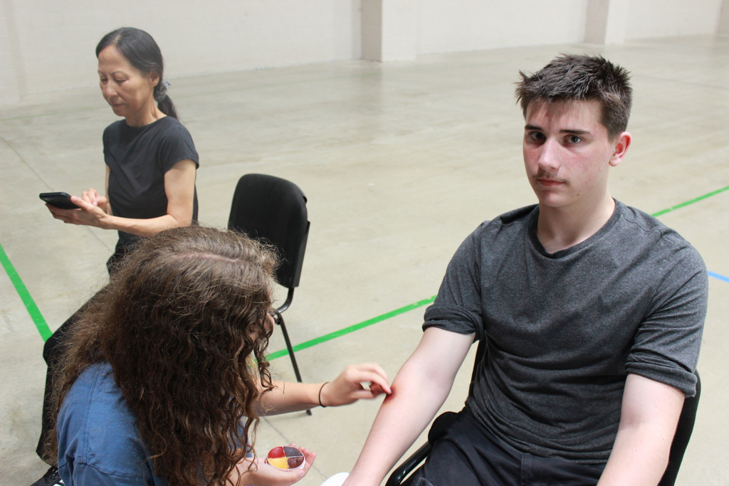 teen boy sitting down while a teengirl applies paint to make it look like a bruise