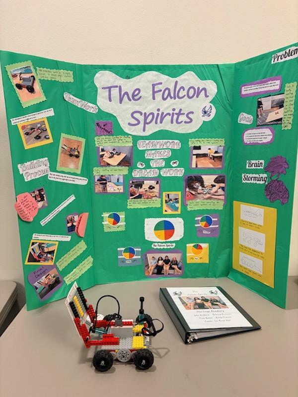 Tri-fold presentation board labeled ‘The Falcon Spirits’ featuring a robotics project process, including photos, diagrams, and brainstorming notes, with a LEGO robot and project binder displayed in front.