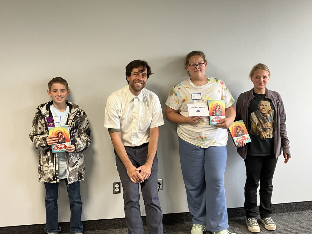 Graphic novelist Ira Marcks with three students holding a copy of his graphic novel Shark Summer