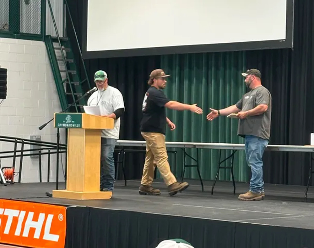 Conservation student receiving award on stage - about to shake one person's hand while another person stands at the podium
