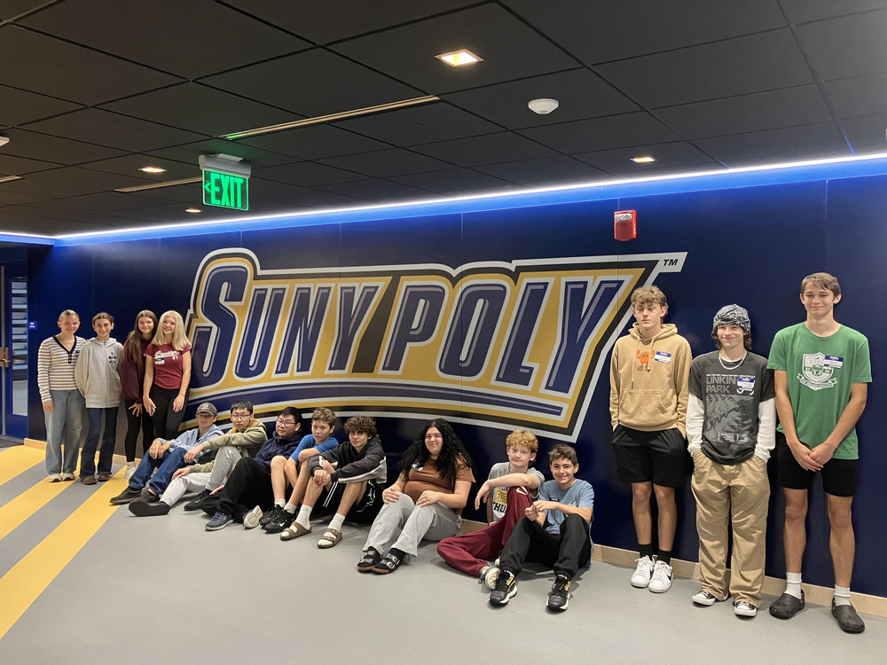 15 students standing by wall decoreated with the words "SUNY Poly"