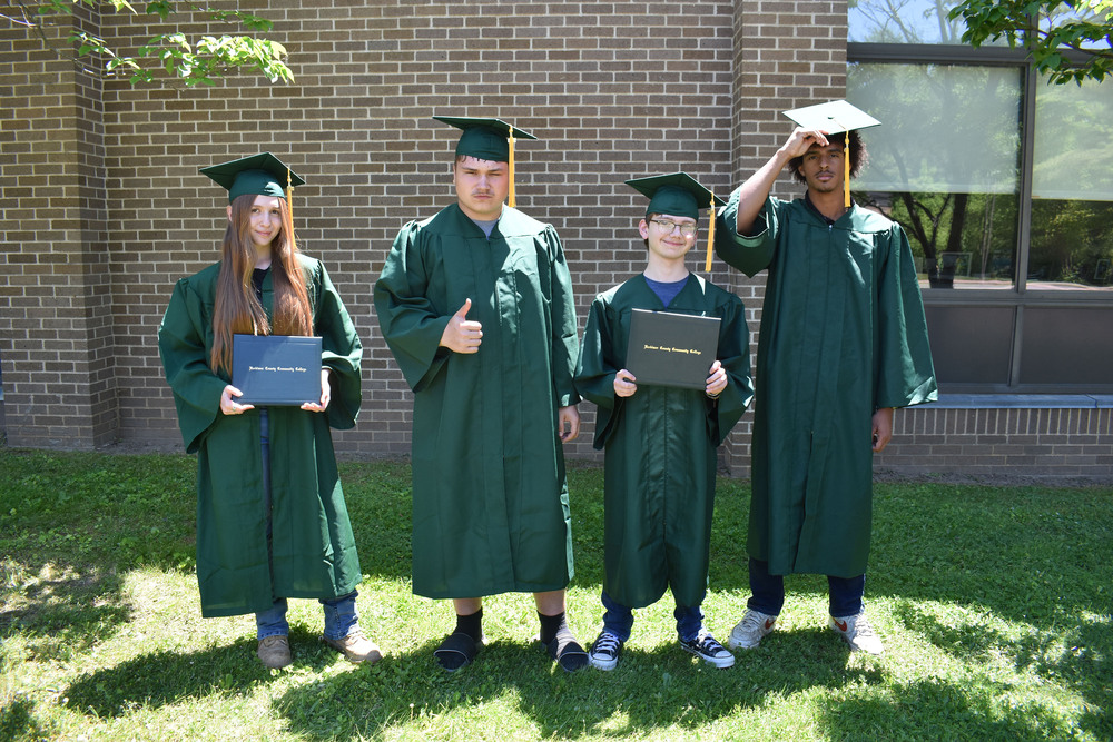 Four VP-TECH students wearing Herkimer College graduation caps and gowns and posing outside of BOCES