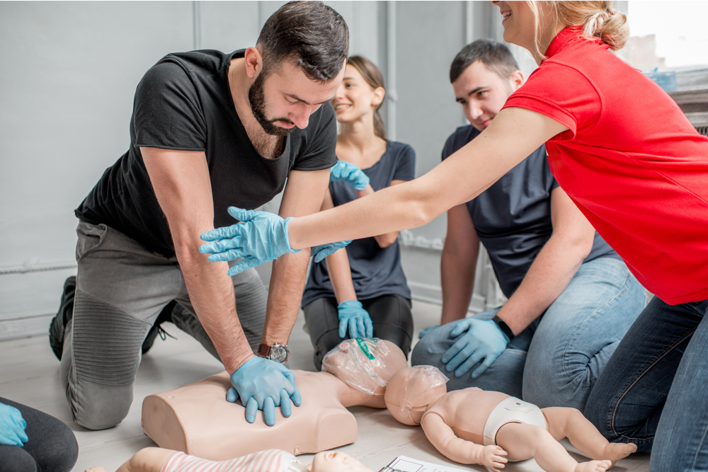 Maining doing CPR on a mannequin with three other people and a baby mannequin nearby