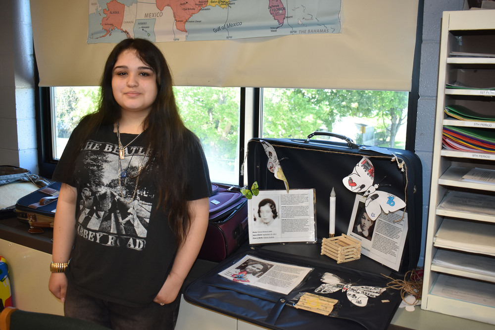 Student posing by suitcase with artwork and proflies of Holocaust victims
