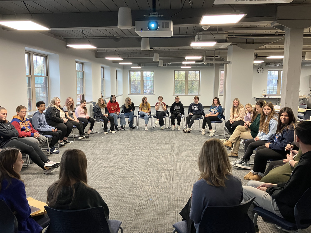 Students sit in chairs in a circle during a workshop
