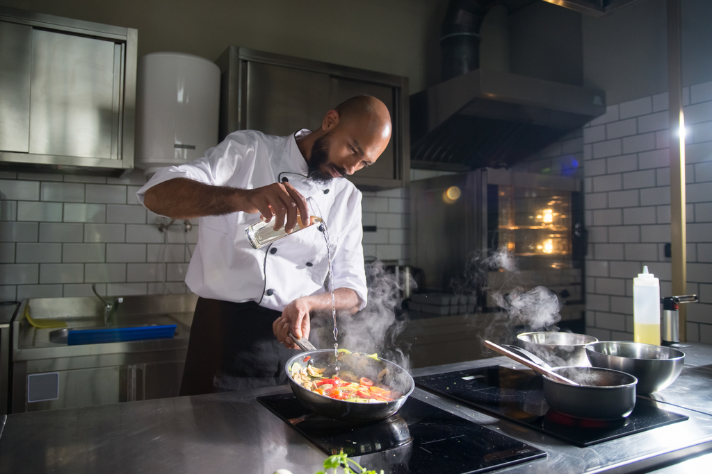 A man pouring a liquid into a frying pan while cooking