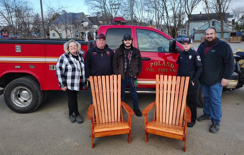 Teaching assistant, fire captain, student, fire safety officer and teacher pose by two Adirondack chairs and a red truck from the Poland Volunteer Fire Co.