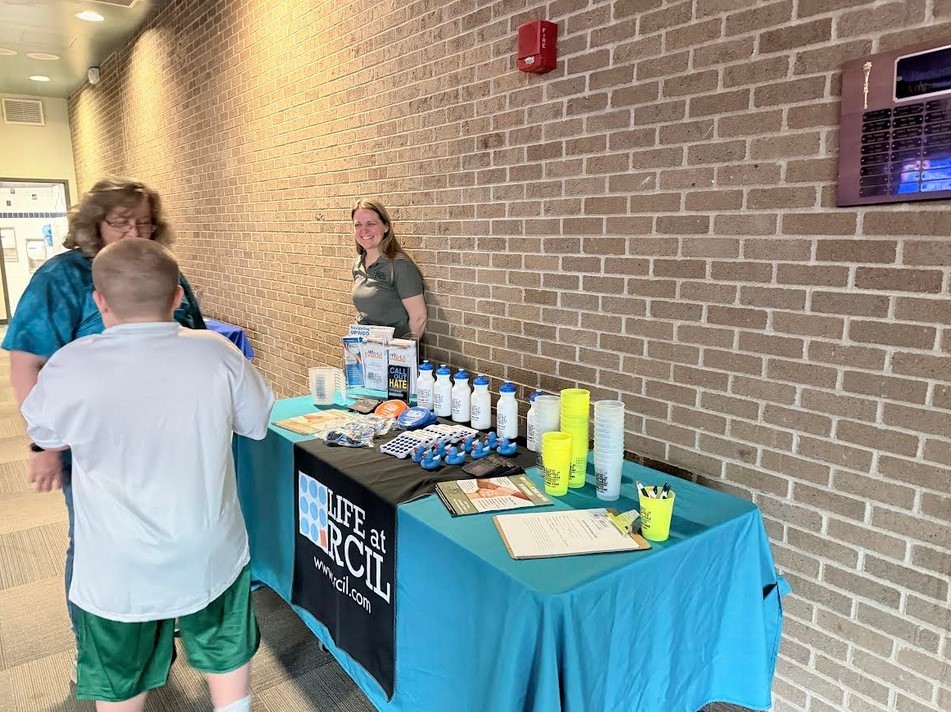 Three people standing buy an RCIL table with various items on it 