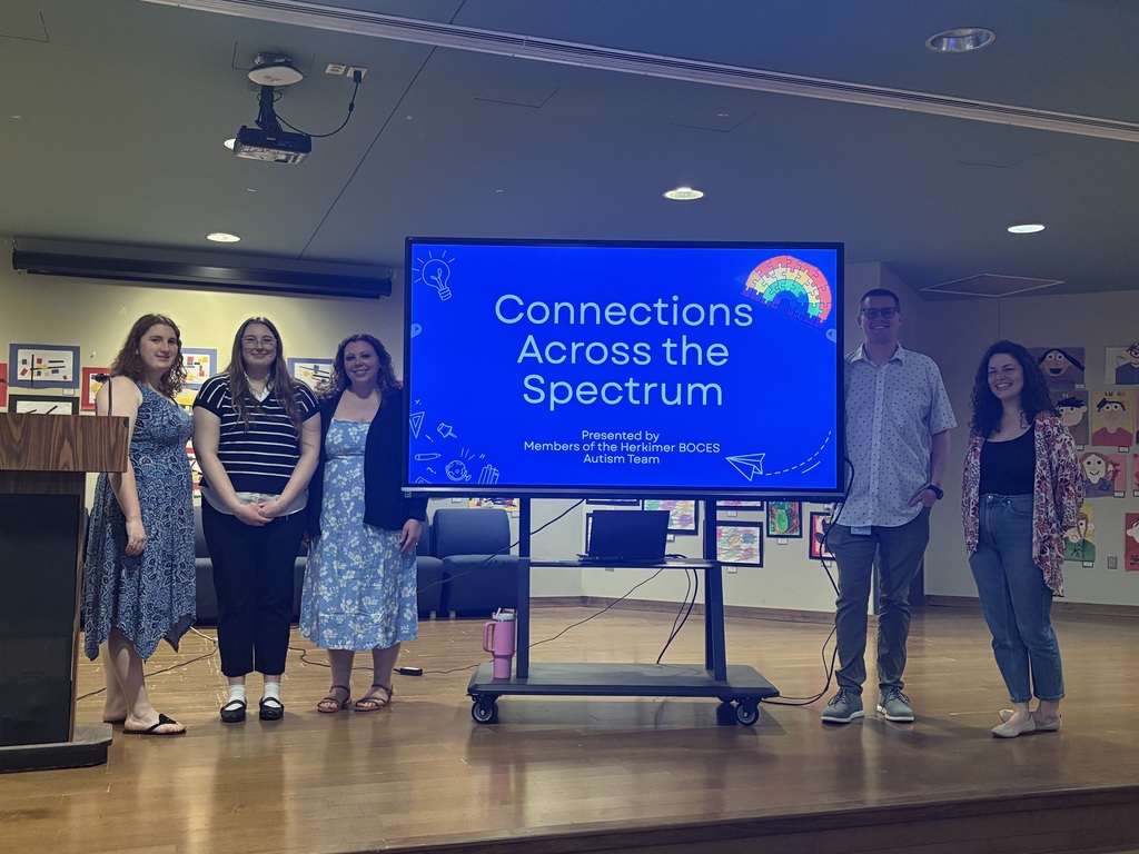 Five people on stage next to a large monitor with the words "Connecting Across the Spectrum"