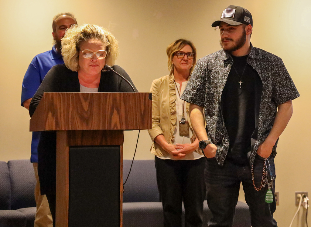 Cheri Evangelista speaks at a podium on stage next to Michael Grecco with Adam Spatto and Tracy Facchini behind them