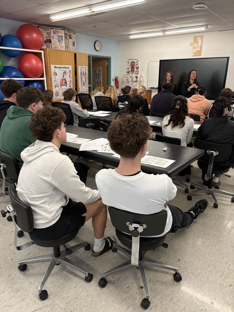 People sitting at tables in a classroom with two people presenting up front