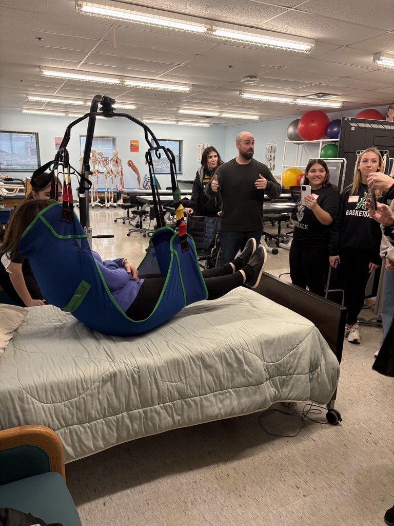 People standing as a lift is used to lower someone into a bed