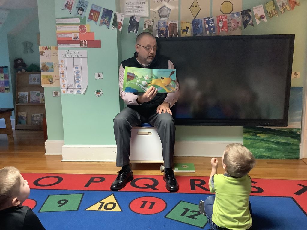 D.J. Shepardson holding a book and reading as two PreK students look on