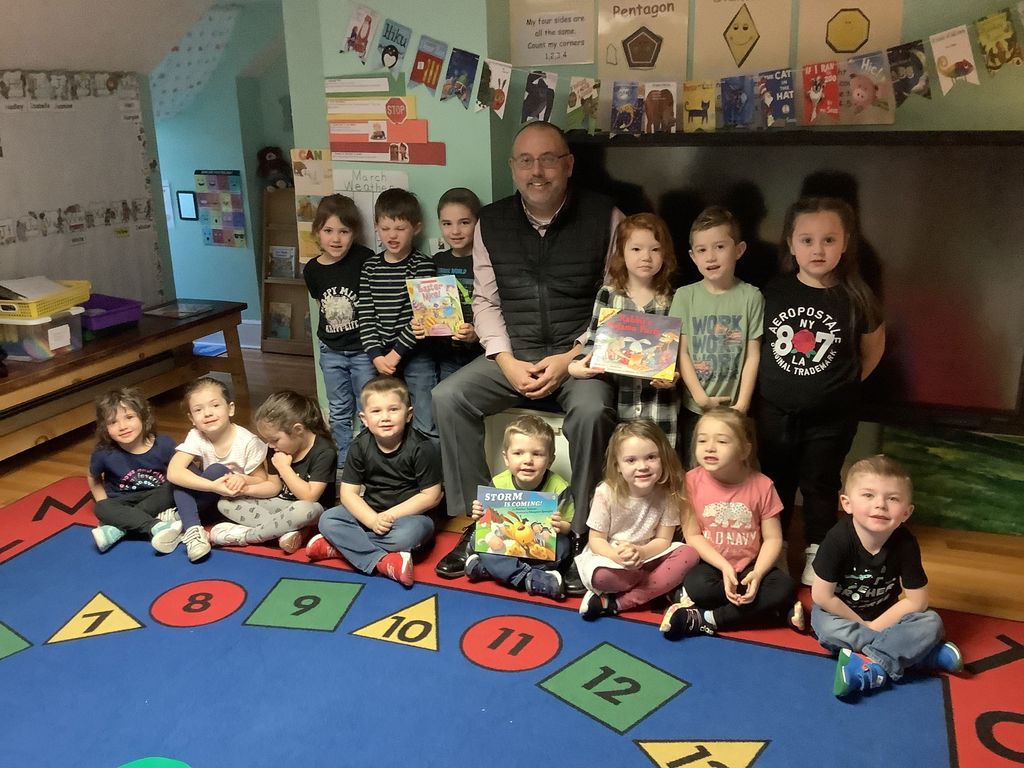 D.J. Shepardson and 14 PreK students posing with books in a classroom