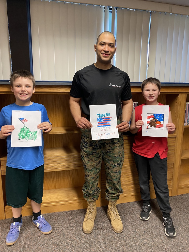 Marine Corps Staff Sgt. Paredes posing with two students and artwork