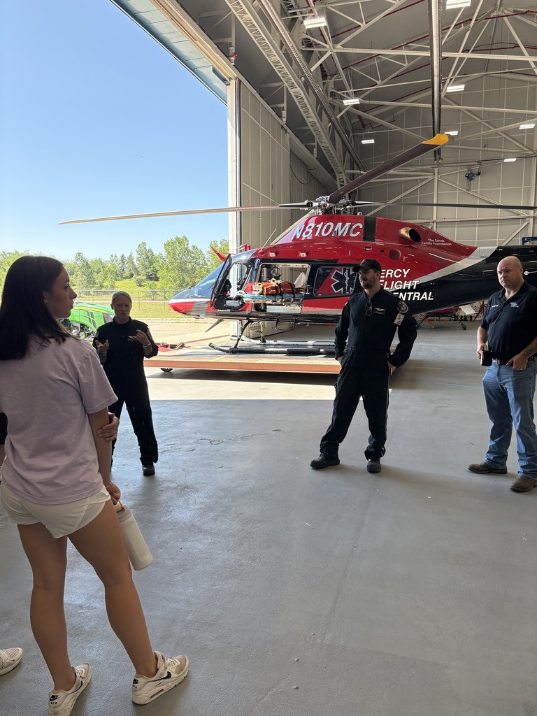 Professionals present to students with a helicopter nearby