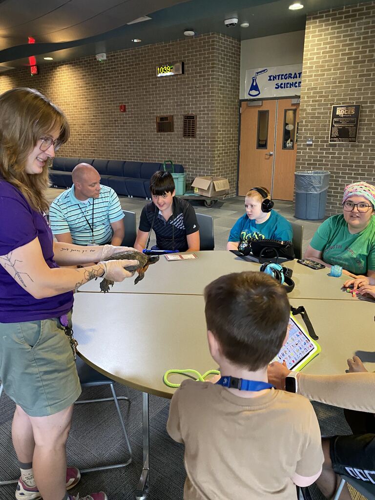 Utica ZooMobile visit to WEB Complex with exhibitor showing a turtle to students and staff at a table
