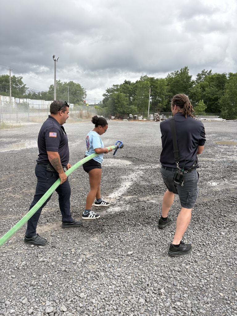 A student spraying a fire hose with two firefighters nearby