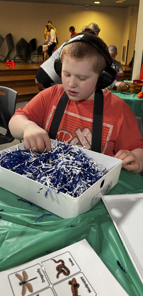 Student wearing headphones participating in an activity with a bin filled with blue and white materials