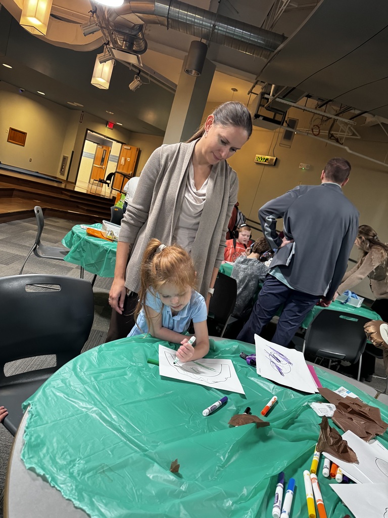 Student doing artwork at a table as staff member looks on