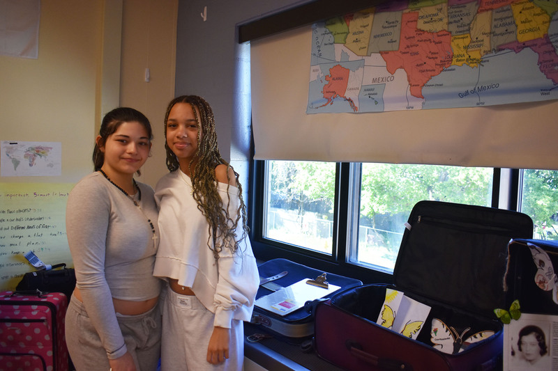Two students posing by suitcase with artwork and proflies of Holocaust victims