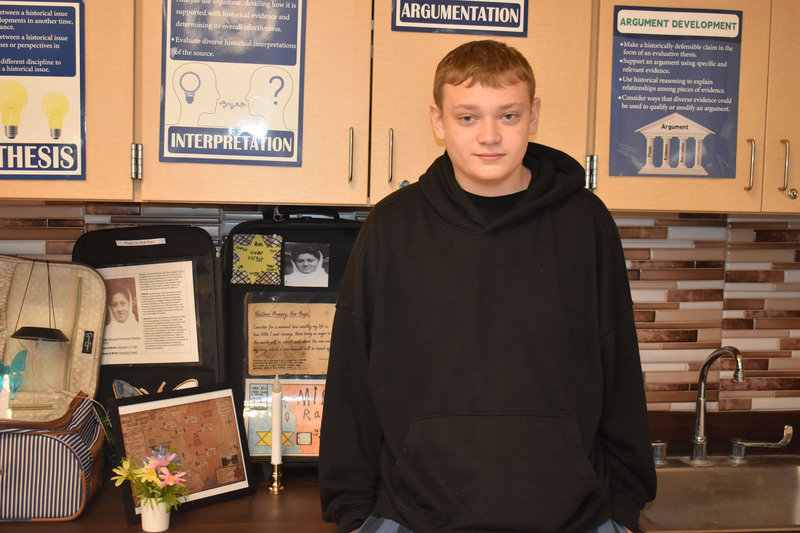Student posing by suitcase with artwork and proflies of Holocaust victims