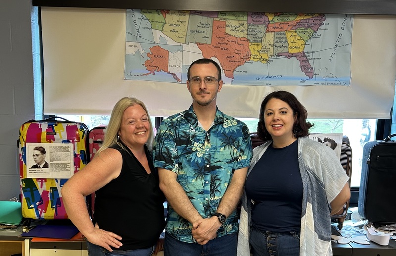 three educators posing together in front of a map in a classroom