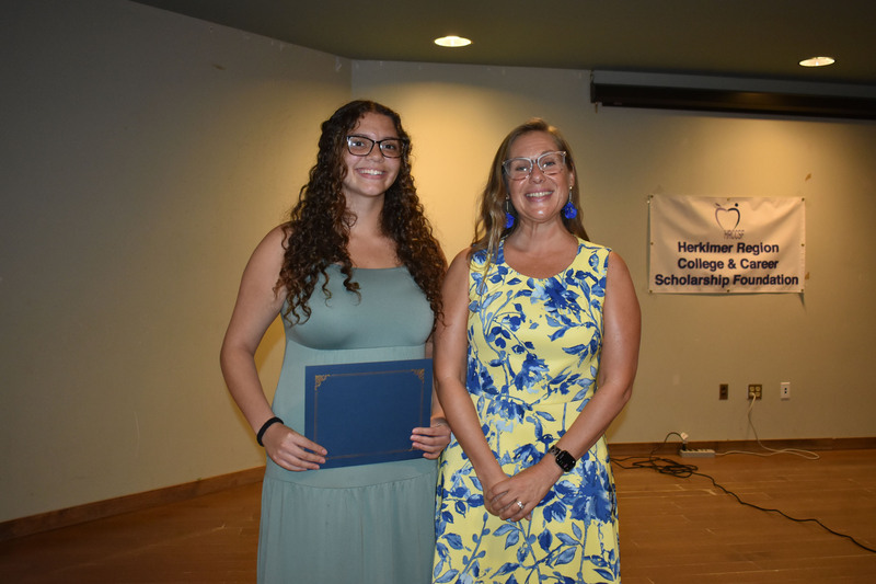 Student on stage holding certificate next to Sarah Crowe