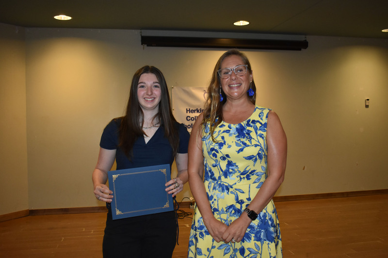 Student on stage holding certificate next to Sarah Crowe